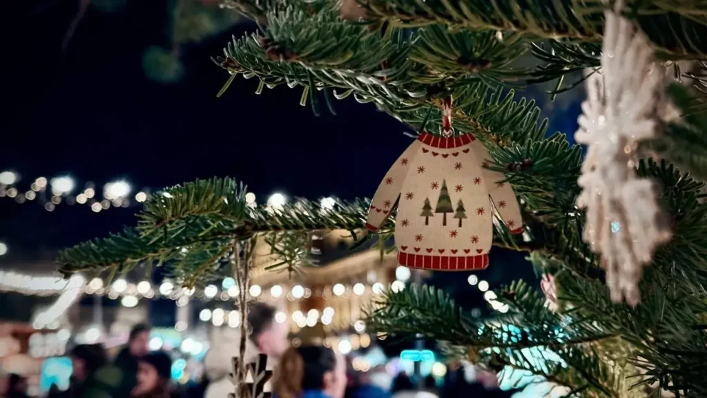 Image of a sweater ornament on a fir tree with holiday lights outside.