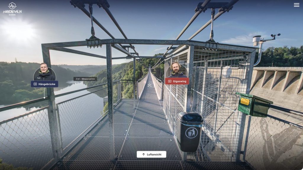 Screenshot of the tour on a metal-grate walkway at the start of a suspension bridge, with hotspots for “Hängebrücke” and “Gigaswing” and a label pointing toward “Ziel – Megazipline.”