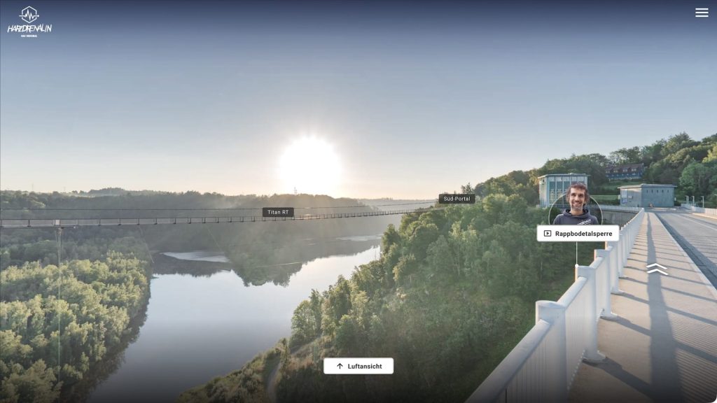 View from the dam walkway in the Harzdrenalin Pano2VR virtual tour overlooking the valley and suspension bridge, with location and video hotspots and an aerial-view toggle.