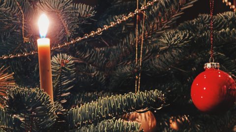 A close up image of a decorated christmas tree with a a candle and bauble.